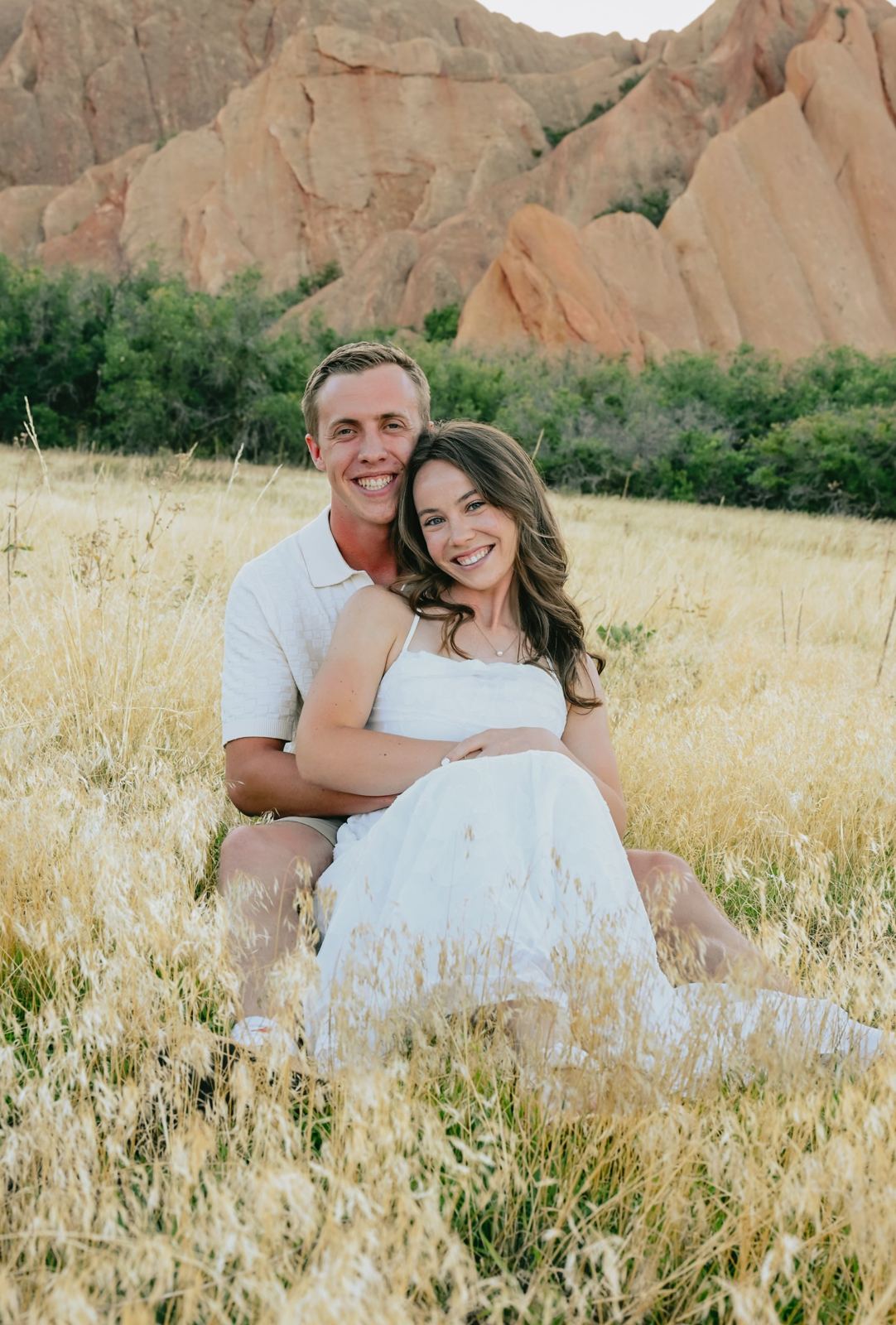 Jacob and Angela sitting together in tall grass in front of red rocks